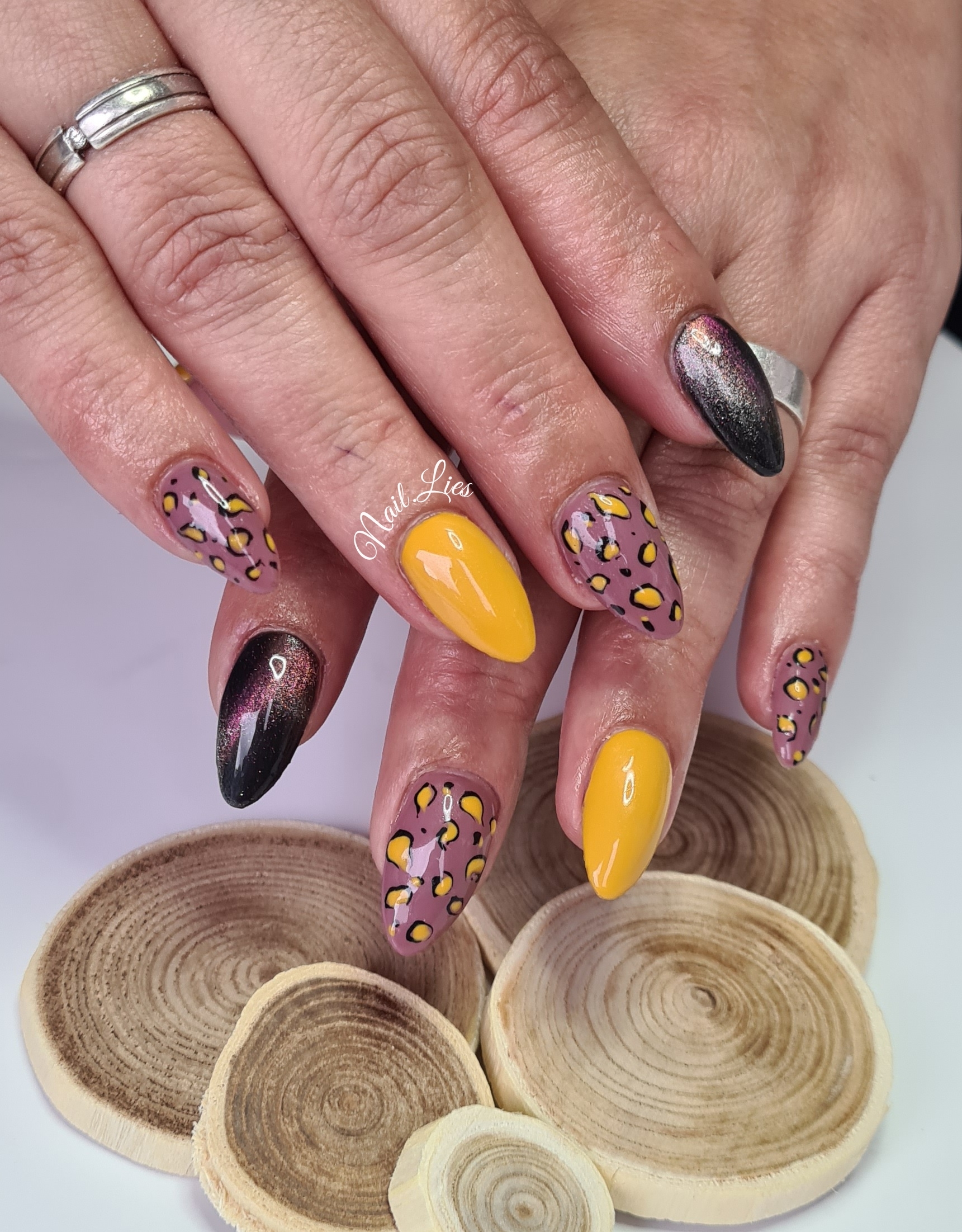 Gele en donkere puntige nagels met luipaardpatronen op een houten ondergrond